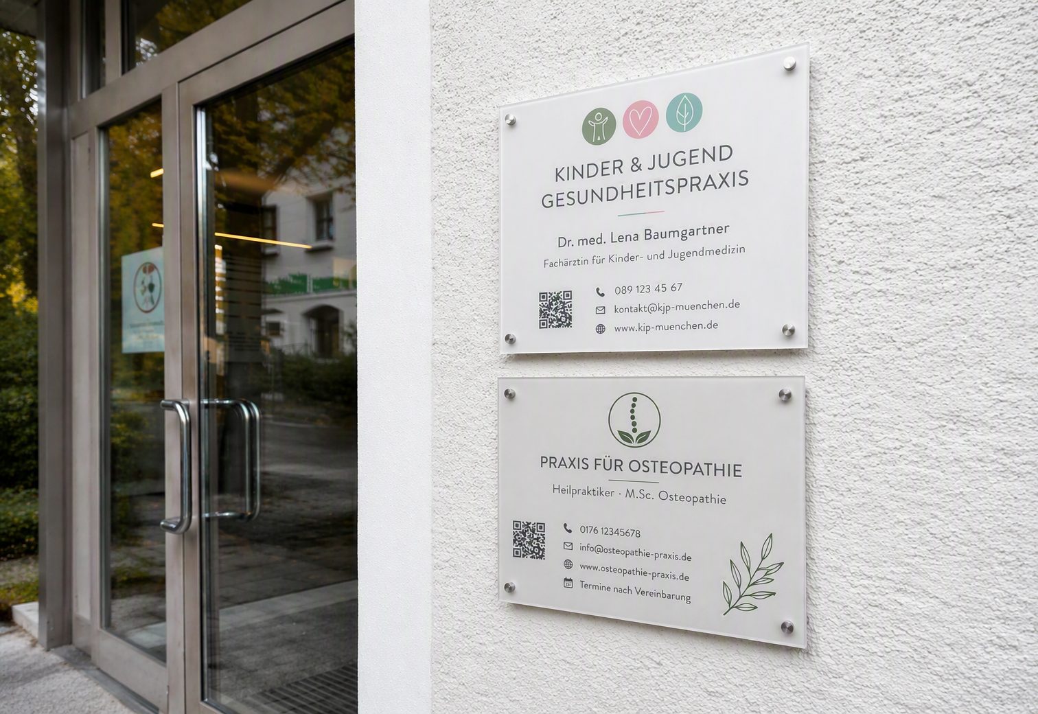 Zwei Praxisschilder aus Acrylglas an einer hellen Außenwand neben einem Eingangsbereich